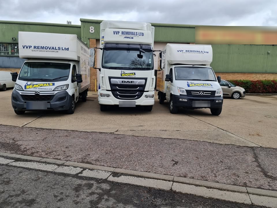 Three white VVP Removals vehicles parked side by side outside a warehouse unit