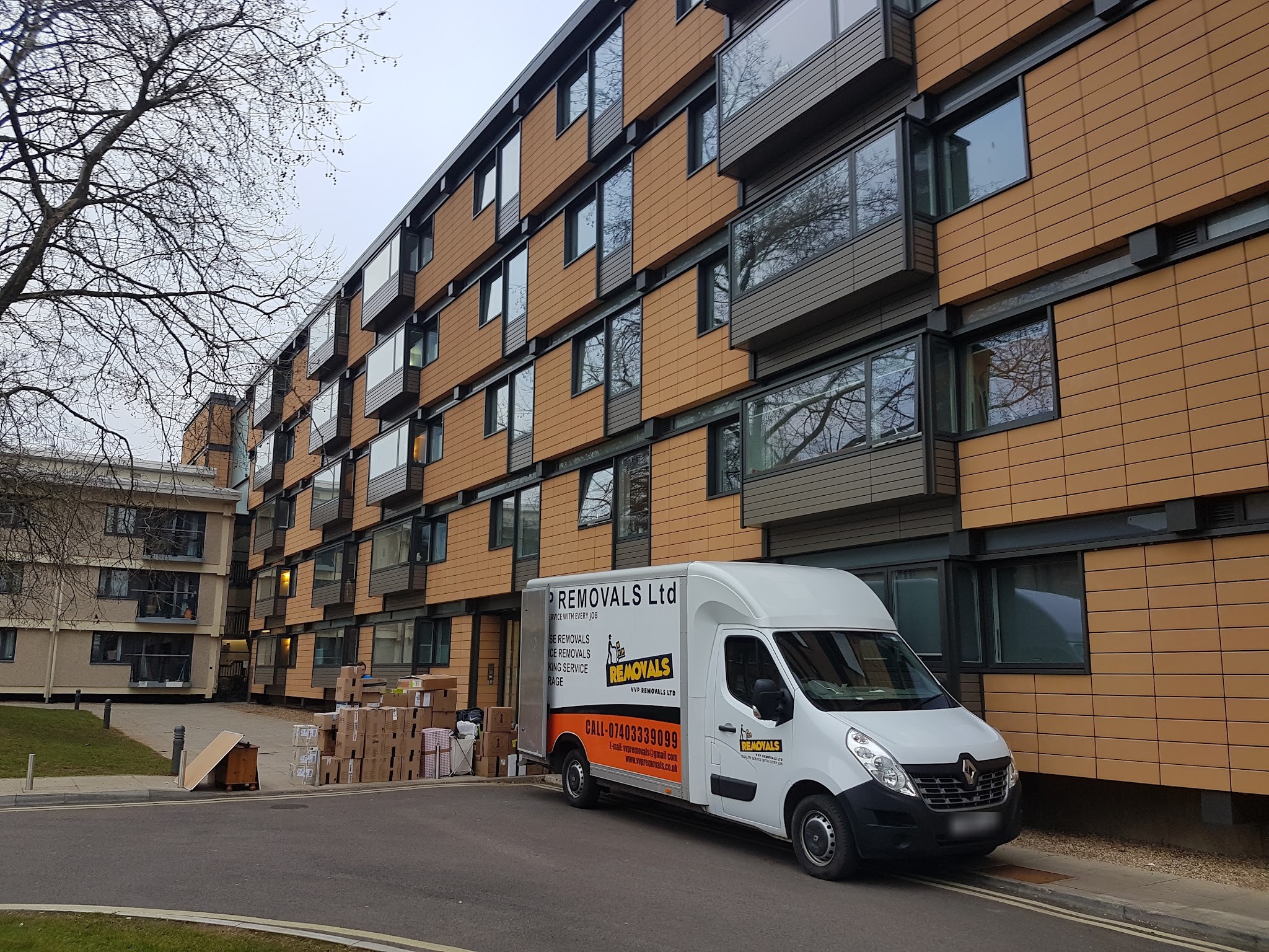 A VVP Removals Luton van parked outside a block of flats, with boxes stacked on the pavement beside it